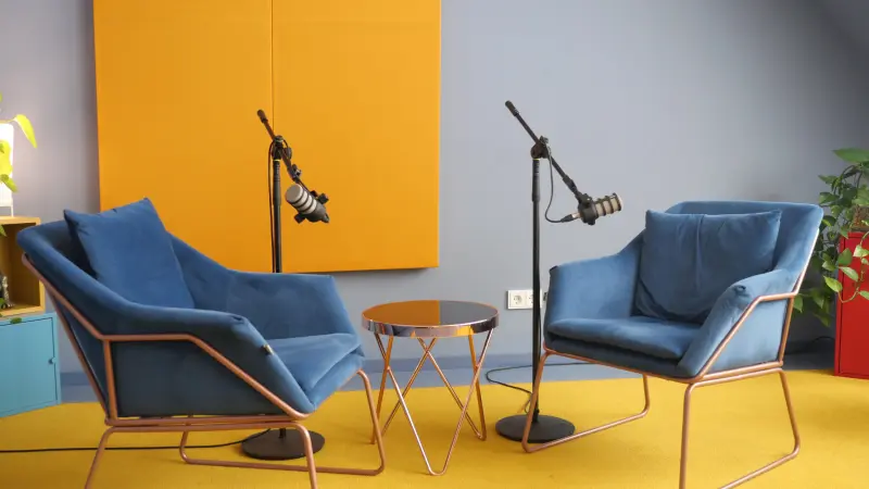 Podcastset mit zwei blauen Sesseln, Mikrofonen vor einer lau/gelben Wand ei Meeet Studios in Berlin Neukölln