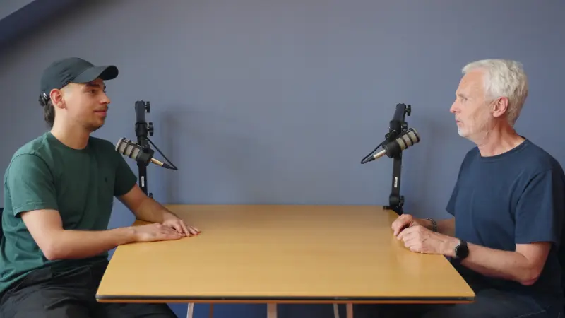 Podcast Set Konrad 1 mit Menschen Totale 800 Podcast-Set im Studio Konrad bei Meeet Studios in Berlin Neukölln: Zwei Personen am Tisch vor hellblauer Wand
